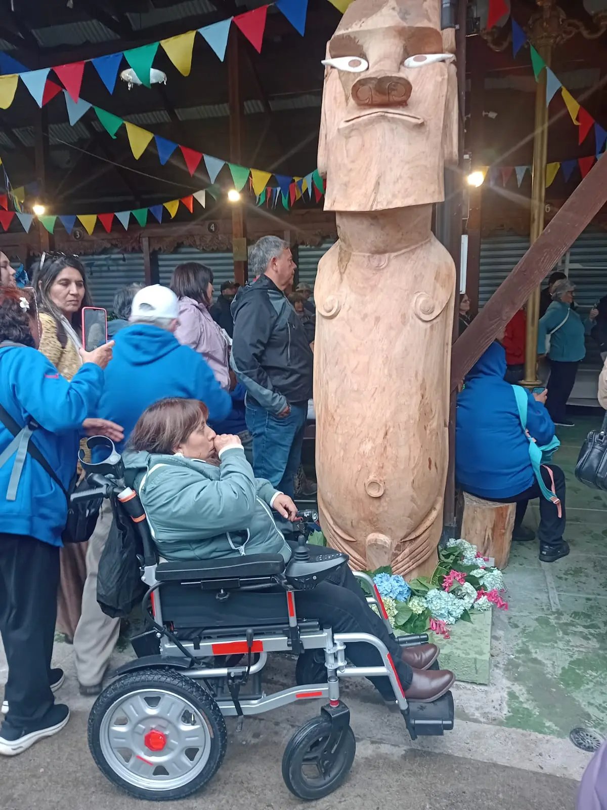 Rapa Nui woman in an electric wheelchair included in a community gathering beside a carved moai
